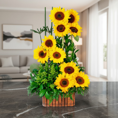 Arreglo floral vertical de girasoles amarillos con follaje verde en base rectangular de madera sobre mesa de mármol en sala moderna