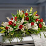 Arreglo de flores sobre un ataúd con lirios blancos, rosas rojas, margaritas blancas y follaje verde