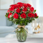 Arreglo de rosas rojas frescas con paniculata blanca en un jarrón de cristal transparente atado con cuerda