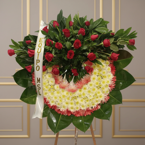 Arreglo fúnebre en forma de corona con rosas rojas en la parte superior y flores blancas y rosas en la parte inferior, sobre base de hojas verdes y cinta con texto Equipo MSL