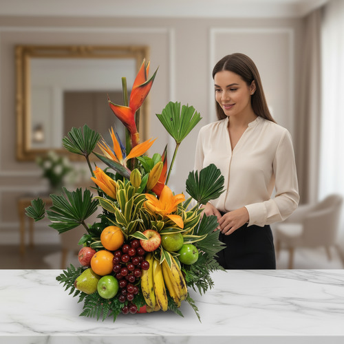 Mujer observando un centro de mesa con frutas tropicales y flores naranjas y rojas sobre una mesa de mármol en una sala elegante