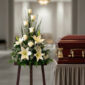 Arreglo floral fúnebre con lirios y rosas blancas junto a un ataúd de madera barnizada en una sala velatoria