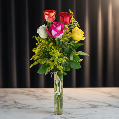 Ramo vertical de rosas rojas, rosadas, blancas y amarillas con follaje verde en un jarrón de cristal sobre mesa de mármol