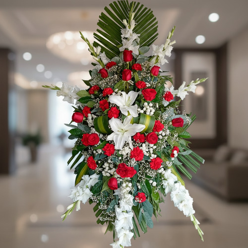 Arreglo floral fúnebre con rosas rojas y lirios blancos Arreglo floral fúnebre en forma ovalada con rosas rojas, lirios blancos y follaje verde sobre fondo de interior elegante desenfocado