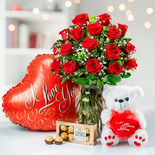 Ramo de rosas rojas en jarrón de cristal junto a globo rojo en forma de corazón con texto I Love You, oso de peluche blanco con corazón rojo y caja de chocolates Ferrero Rocher