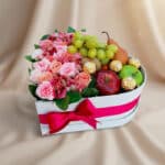 Arreglo AMOS en caja corazón con rosas rosadas, alstroemerias, uvas, manzanas, pera y chocolates Ferrero Rocher, ideal para r