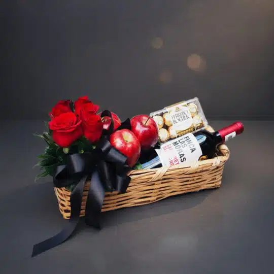 Arreglo ANGELO: Elegante cesta de mimbre con rosas rojas frescas, manzanas rojas, botella de vino tinto Finca Las Moras y caj