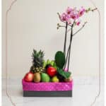 Arreglo ANTONELLO con orquídea Phalaenopsis rosa y frutas frescas como piña, manzanas, kiwis y mangos, presentado en una caja