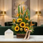 Arreglo floral de lujo con girasoles vibrantes, exóticas aves del paraíso y follaje verde, presentado en una cesta de mimbre