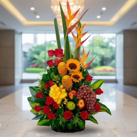 Arreglo floral premium con rosas rojas, girasoles, aves del paraíso, frutas durio, uvas y manzanas, sobre mármol en un lobby