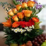 Primer plano extremo del Arreglo Floral con Frutas Hadar, mostrando rosas naranjas, gerberas rojas y margaritas blancas con g