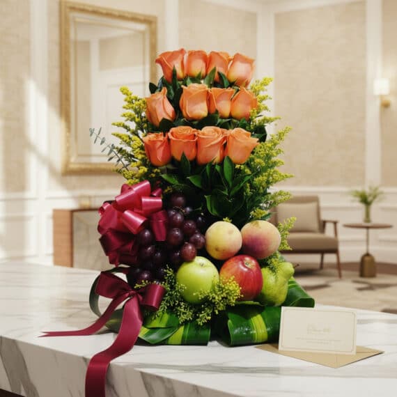 Arreglo floral de rosas color salmón con uvas, manzanas, duraznos y peras, decorado con cinta de satén burdeos sobre una mesa