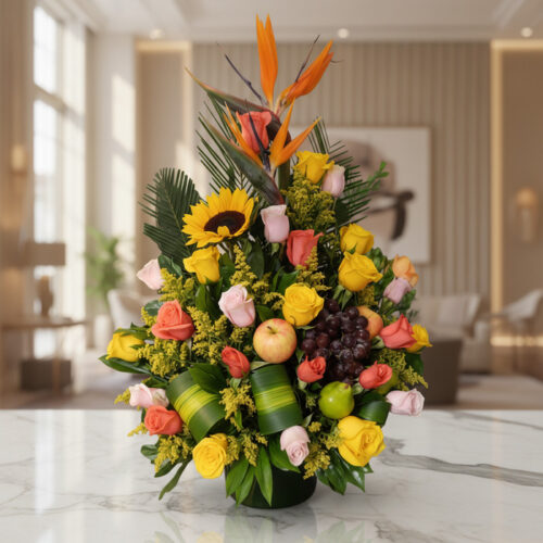 Arreglo floral vibrante con rosas amarillas y salmón, girasol, ave del paraíso y frutas tropicales como uvas, manzana y lima,