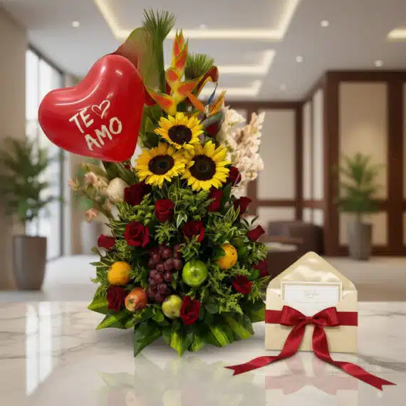 Arreglo floral con girasoles, rosas rojas, frutas tropicales, globo de corazón 'Te Amo' y tarjeta de regalo en un entorno ele