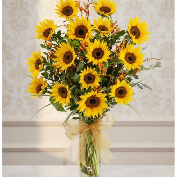 Arreglo floral de girasoles LENU en un jarrón de cristal con lazo dorado, sobre una mesa de mármol y fondo elegante.