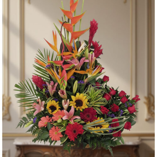 Arreglo floral IDARA con rosas rojas, girasoles, lirios, heliconias y jengibre rojo en un fondo elegante y bien iluminado.
