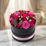 Arreglo floral LILIAN en caja negra con cinta rosa, lleno de rosas lila y rojas, ideal para regalar.