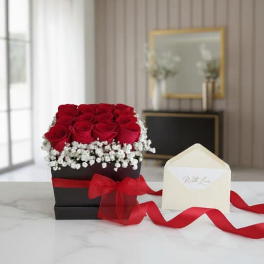 Arreglo Floral Pétalos con rosas rojas frescas y gypsophila en una caja cuadrada negra con cinta roja, sobre una mesa de márm