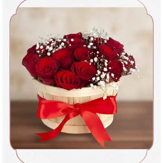 Arreglo floral 'Lidia' con 15 rosas rojas premium en un balde rústico de madera, adornado con un lazo rojo y follaje blanco,