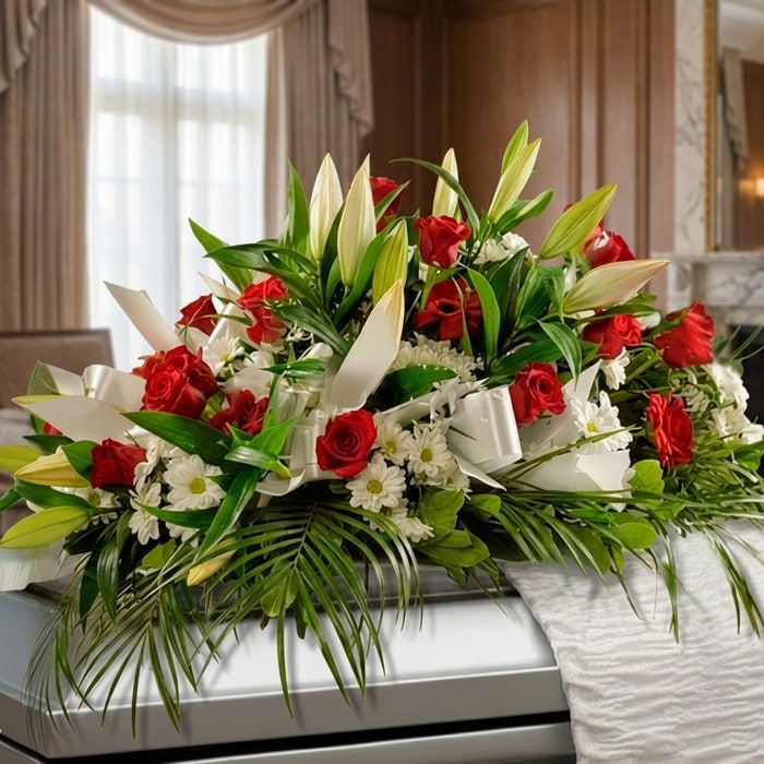 Arreglo fúnebre cubre caja Paraíso con rosas rojas, lirios blancos y margaritas, sobre un ataúd en una sala de velación premi