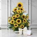 Impresionante arreglo floral con girasoles vibrantes, follaje verde y un lazo de satén, presentado sobre una mesa de mármol.