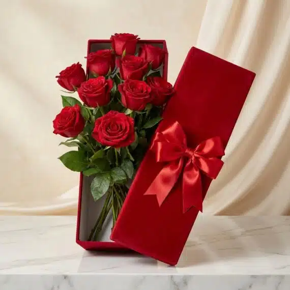Arreglo de Rosas Maira: Caja Premium con 12 Rosas de Exportación Caja premium de terciopelo rojo con 12 rosas rojas de exportación, frescas y con gotas de rocío, sobre una mesa de mármol bla
