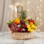 Canasta de mimbre con frutas frescas variadas como piña, uvas, manzanas, kiwis, naranjas, peras, fresas y plátanos, decorada