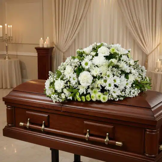 Cubre caja fúnebre Epifania con flores blancas y verdes sobre un ataúd de caoba brillante en una sala de velación de lujo.