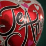 Primer plano extremo de un globo metalizado rojo y blanco con la frase 'Te Amo' en negro, cubierto de sutiles gotas de rocío