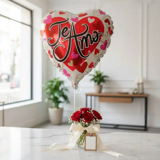 Globo metalizado en forma de corazón con la frase 'Te Amo' flotando sobre un arreglo de rosas rojas frescas en un jarrón de c