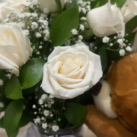 Primer plano extremo de un arreglo floral 'Jarrón Llévame Contigo' con rosas blancas, gotas de rocío sutiles y follaje verde,