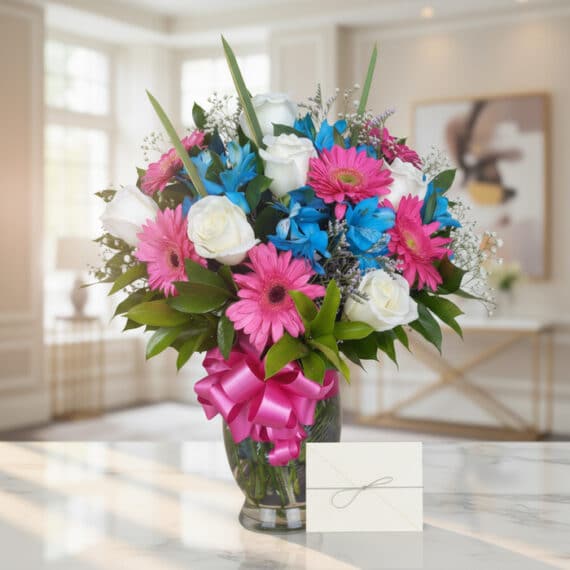 Jarrón Primavera con rosas blancas, gerberas fucsia y alstroemerias azules, sobre una mesa de mármol en un ambiente luminoso