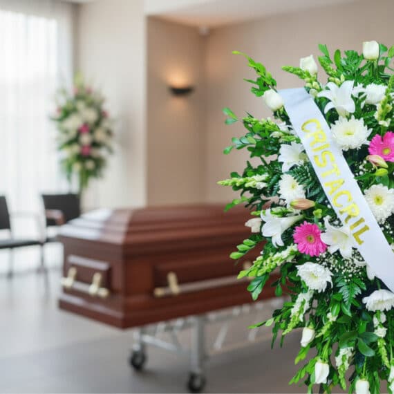 Pedestal fúnebre Sagrado con flores blancas y fucsias, cinta personalizada, en primer plano de una sala de velación moderna c