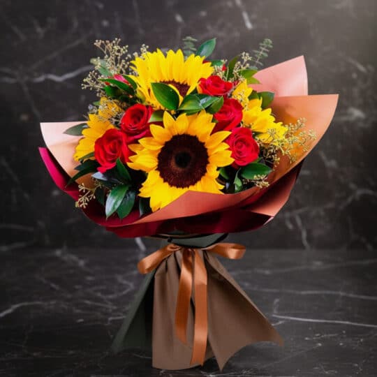 Ramo Aurora de rosas rojas y girasoles vibrantes, envuelto elegantemente en papel de tonos tierra y atado con un lazo de saté