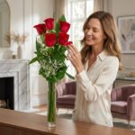 Mujer elegante admirando un Solitario con Rosas Marilyn en un jarrón de cristal, en un interior de hogar de alto diseño con l